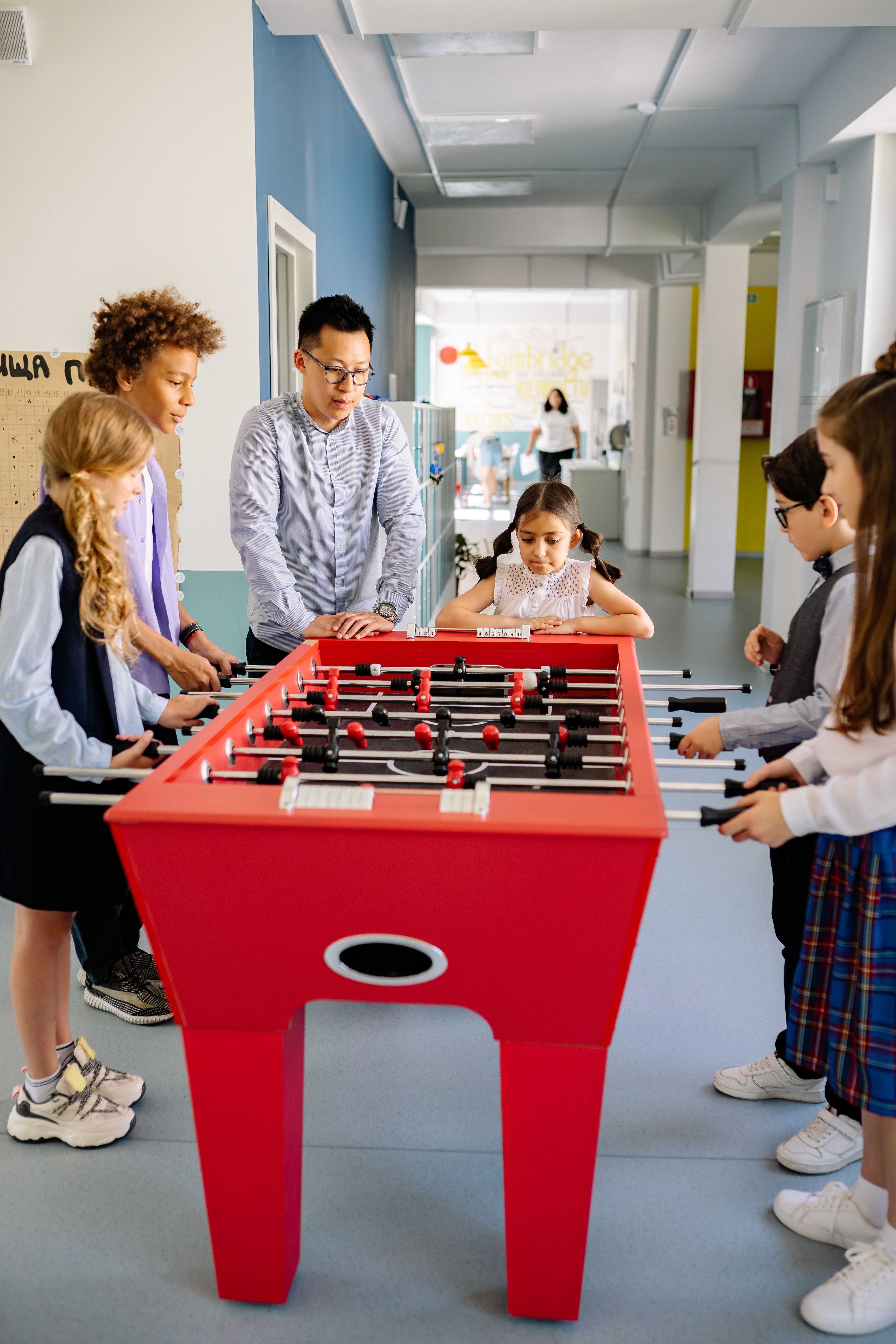 Children playing table football at after school club with teacher - Ofsted expects age-appropriate activities and adequate supervision in after school clubs